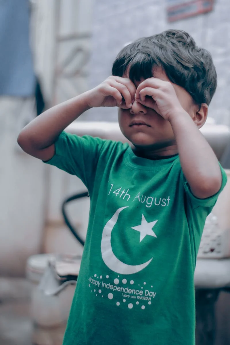 Young boy in a green Pakistan Independence Day shirt making a binocular gesture with his hands.