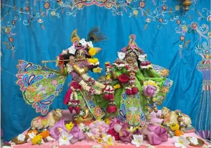 Beautifully decorated Murtis (deities) of Radha and Krishna, adorned with flowers and peacock feathers for a Janmashtami celebration.